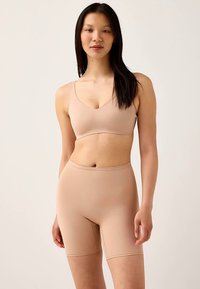 Beige naadloze bralette en shorts met hoge taille van glad, rekbaar stof. Heeft een ronde halslijn en een ontwerp tot aan de knieën.