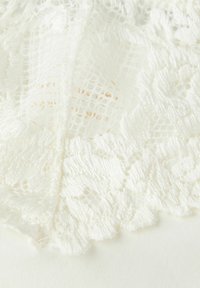 Vitt spetstyg med ett blommönster, som har intrikata, scallop-patterns kanter. Texturen är mjuk med en delikat, luftig framtoning.