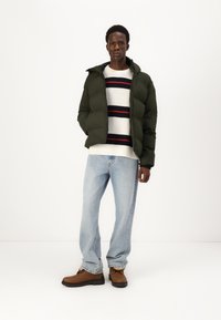 Grøn pufferjakke med hætte, hvid sweater med marineblå og røde striber, lyseblå jeans og brune støvler. Simpelt, afslappet design.