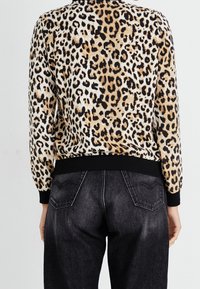 Sweater med leopardtrykt, fremstillet af et blødt materiale, med sorte ribbede manchetter og kant og en tætsiddende silhuet, parret med mørkvaskede jeans.