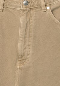 Beige denimbukser med en frontlomme og søm detaljer. Har en metalknap og en tekstureret overflade.