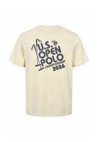 T-shirt beige avec des motifs de maillet de polo noirs et le texte "U.S. Open Polo Championship 2026" au dos.