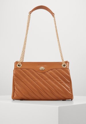 Un sac à main en cuir marron avec des coutures diagonales, une bandoulière en chaîne dorée et un fermoir à torsion sur un piédestal blanc contre un fond uni.