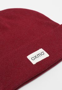 Burgundy knit beanie hat with a soft texture and a stitched white label displaying "oxmo." The design is simple and close-fitting.