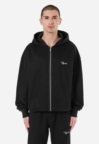 Black corduroy zip-up hoodie with a large hood, front pockets, and embroidered logo on the left side. Soft texture and relaxed fit.