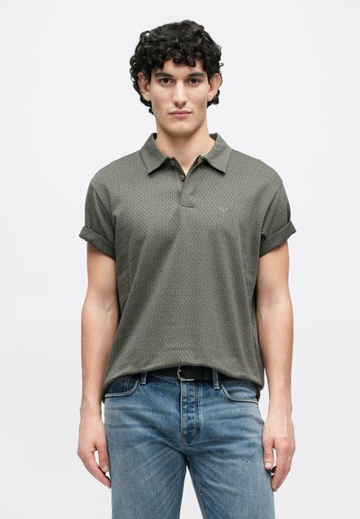 Polo vert foncé avec un motif texturé, manches retroussées et un plastron à deux boutons. Assorti à un jean en denim bleu.