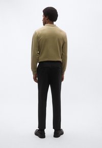 Πόλο μπλούζα μακρυμάνικη σε ελιά πράσινο χρώμα με γιακά, συνδυασμένη με μαύρο παντελόνι και μαύρα παπούτσια. Λείο ύφασμα, ραμμένη εφαρμογή.