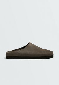 Chausson en daim gris à enfiler, à bout fermé, avec semelle noire, présenté de profil sur fond uni.