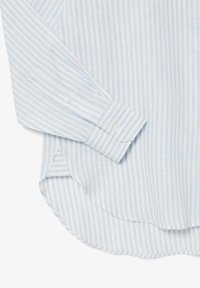 Camisa de manga larga a rayas azul claro, hecha de una tela suave. Presenta puños abotonados y un dobladillo curvado, con una textura sutil visible en el material.