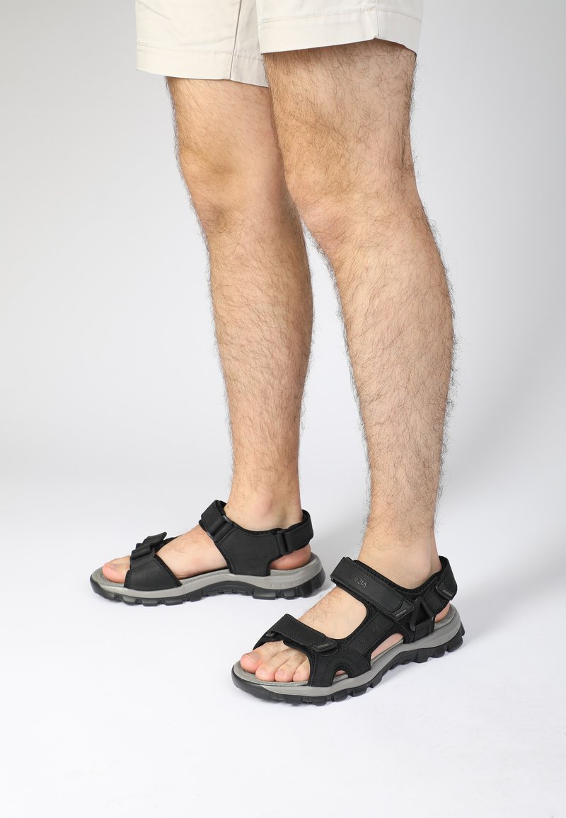 Sort sandal med justerbare stropper, tekstureret gummisål, åben tå-design og grå accenter. Velegnet til afslappet brug eller udendørs aktiviteter.