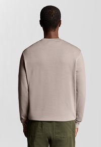 Lange mouw sweatshirt in lichtbeige, gemaakt van soepel materiaal, met een ronde hals en geribbelde manchetten, gedragen met olijfgroene broek.