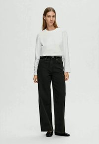 Jeans largos pretos de cintura alta, combinados com uma camisa ajustada de mangas longas branca. O tecido parece suave, com textura mínima.