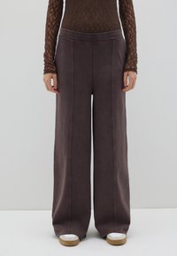 Pantalones de pierna ancha en un tejido gris oscuro, con una textura suave, cinturilla elástica y costuras verticales, combinados con zapatillas blancas y marrones.