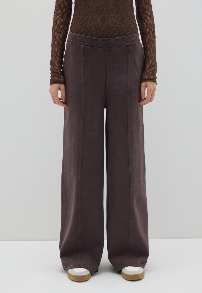 Pantalones de pierna ancha en un tejido gris oscuro, con una textura suave, cinturilla elástica y costuras verticales, combinados con zapatillas blancas y marrones.