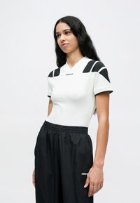 Weißes Sportshirt mit schwarzen Akzenten an Schultern und Ärmeln, kurzärmelig, kombiniert mit schwarzen, locker sitzenden Hosen, mit Logodetail.