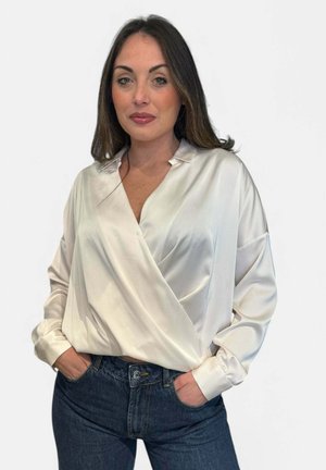 Blusa avvolgente bianca in satin con scollatura a V e maniche lunghe, abbinata a jeans blu scuro. Texture liscia e dettagli di design minimalisti.