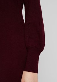 Bordeauxn punoinene neulepaita, jossa on hienoa neulosta, lievästi puffattu muotoilu ja koristeompeleet hihansuussa.