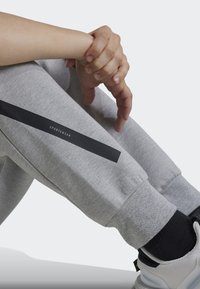 Szürke melegítőnadrág fekete csíkkal, rajta a "SPORTSWEAR" felirattal. Puha tapintás, keskenyedő mandzsetták, fekete zoknikkal és fehér sportcipőkkel párosítva.