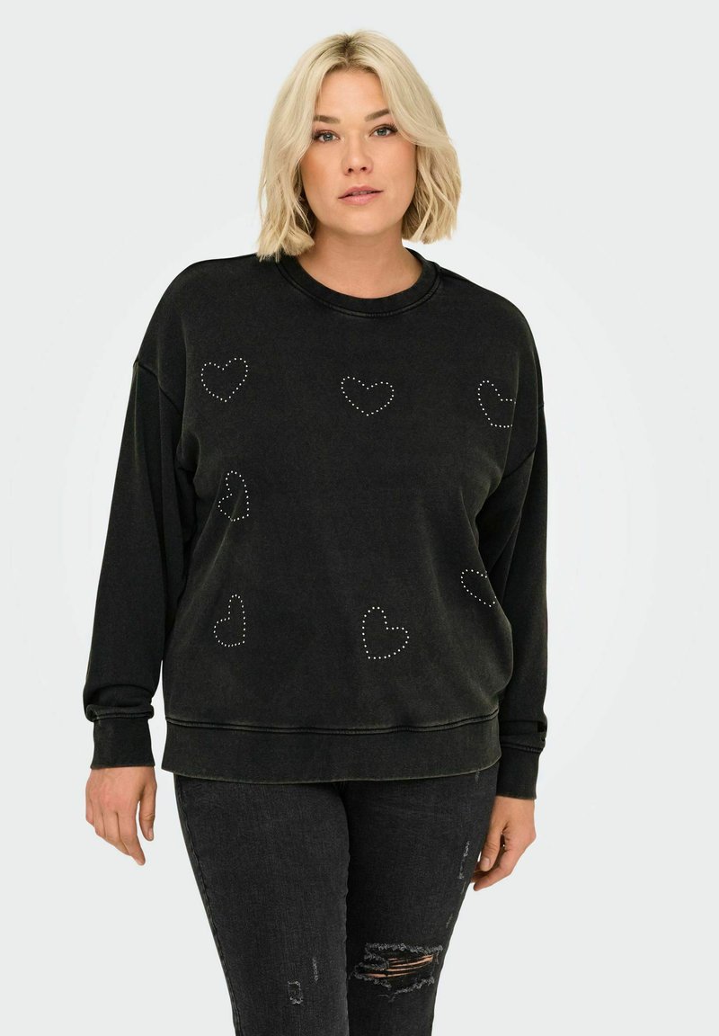 Svart sweatshirt med avslappnad passform, rund halsringning och sydda hjärtdesigner i silver nitar över framsidan. Slitna jeans kompletterar outfiten.