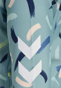 Akvafärgad tyg med abstrakta penseldrag i marinblått, mintgrönt och persika. Innehåller vita chevrondetaljer på ärmen.