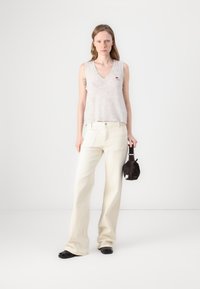 Top de punto sin mangas en gris claro con escote en V y parche de logo, combinado con pantalones de pierna ancha en color crema y un bolso pequeño negro. Zapatos planos negros.
