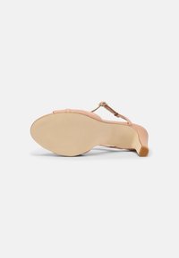 Nude high-heeled sandal with a smooth leather upper, adjustable ankle strap, and a curved heel. The sole is beige with subtle grooves.