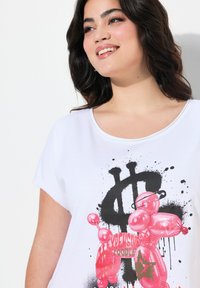 T-shirt bianco a maniche corte con grafica di un cane palloncino rosa, dettagli con macchie nere e un design con il simbolo del dollaro. Materiale in cotone morbido.