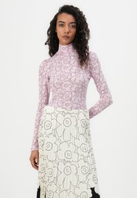 Rosa Langarmoberteil mit Blumenmuster; hoher Kragen. Cremefarbener Faltenrock mit schwarz umrandeten Blumen, fließendes Design.