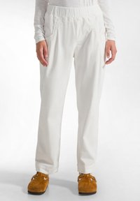 Witte corduroy broek met gestructureerde strepen, elastische tailleband en zijzakken. Losse pasvorm, tapered leg design, aangevuld met bruine slippers.