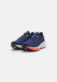 Baskets de sport bleues avec tige en mesh, accents noirs et semelle intermédiaire blanche avec un détail orange au niveau du talon. Semelle en caoutchouc pour une meilleure adhérence.