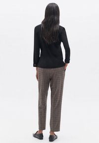 Maglietta nera a manica lunga, pantaloni grigi a quadri e scarpe nere slip-on. La maglietta ha un design aderente e i pantaloni presentano una vestibilità affusolata.