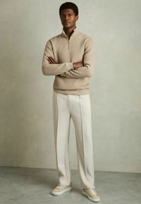 Beige ribbet sweater med zip-krave, parret med lyse creamfarvede skræddersyede bukser og beige sneakers. Glat tekstur og neutral farveskema.
