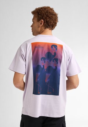 T-shirt en coton violet arborant un graphique coloré de flamants st stylisés au dos, avec des nuances dégradées d'orange et de bleu.