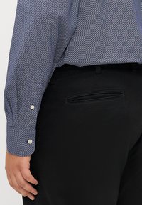 Niebieska koszula z długim rękawem w wzór diamentowy, połączona z czarnymi spodniami. Posiada białe guziki przy mankietach oraz detal z tylnej kieszeni.