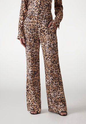 Mujer con pantalones de pierna ancha y talle alto y camisa de manga larga a juego con estampado de leopardo en tonos marrón claro y negro, con sandalias abiertas.