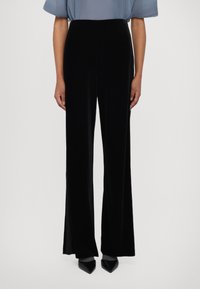 Pantalons larges en velours noir avec une texture lisse. Présentent une taille haute et sont associés à un haut plissé bleu clair et des talons aiguilles.