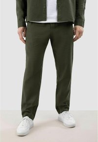 Groene linnen broek met een rechte pasvorm, gecombineerd met witte sneakers. De stof heeft een gestructureerde uitstraling met een subtiele glans.