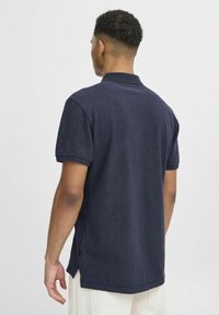 Tumši zilā krāsa polo krekls, izgatavots no mīksta, struktūrēta auduma. Tam ir klasiskā apkakle, īsas piedurknes un sānu šķēlumi apakšmalā.