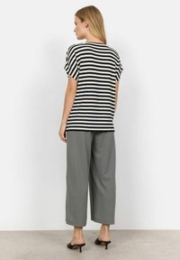 Sort-hvid stribet kortærmet t-shirt parret med løse grå bukser, båret med sorte hæle. Ensfarvet hvid baggrund.