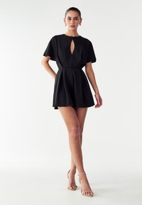 Črn kratek romper z okroglim ovratnikom in detajlom ključavnice. Ima kratke rokave, oprijet pas in široko krilo. Gladka tkanina.