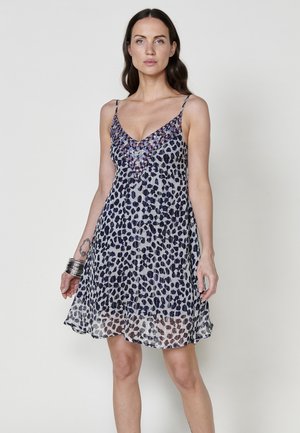 Une robe sans manches avec un décolleté en V, ornée d'un motif léopard bleu marine et blanc, en tissu fluide et avec un ourlet superposé en texture transparente.
