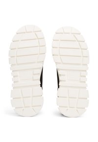 Baskets noires avec une tige en tissu texturé, dotées d'une semelle en caoutchouc blanche avec de profondes rainures pour la traction, et un détail de marque subtil.