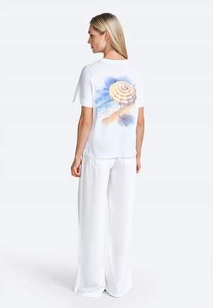 White short-sleeve t-shirt with a colorful watercolor print of a beach umbrella on the back; paired with wide, flowing white pants.