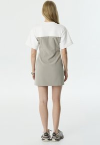 Grijs-witte korte jurk met een aansluitend ontwerp, korte mouwen en een rechte zoom. Gekozen met gemusterde sneakers. Minimalistische stijl.