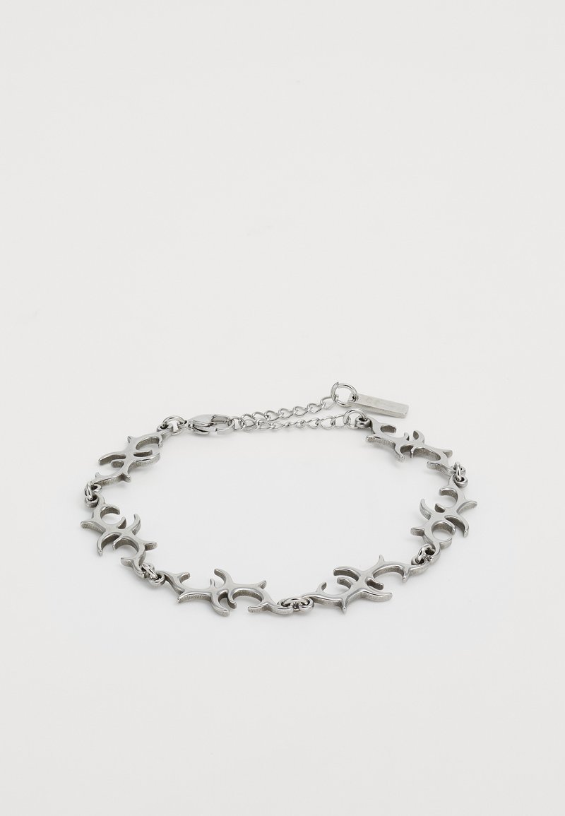 Silver metal bracelet with connected abstract tribal-style links and a small rectangular tag near the clasp on a white background.