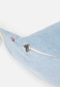 Cuscino in denim a forma di balena di colore azzurro chiaro, con chiusura a zip e tirante in metallo. Etichetta rossa visibile sul lato. Texture morbida.