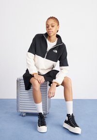 Black and cream zippered pullover jacket with a high collar, paired with a black skirt and platform sneakers. Textured fabric, casual fit.