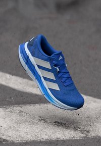 Blauer Laufschuh mit strukturiertem Obermaterial, drei weißen Streifen und leichter Sohle. Verfügt über einen gepolsterten Kragen und kontrastierende Akzente.