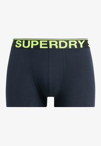 Boxer shorts en coton bleu marine avec une taille noire arborant un texte jaune vif qui indique "SUPERDRY". Texture lisse, coupe ajustée.