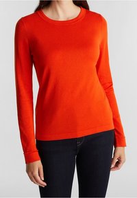 Red long-sleeve sweater made of soft knit fabric, featuring a round neckline and ribbed cuffs, paired with dark jeans.